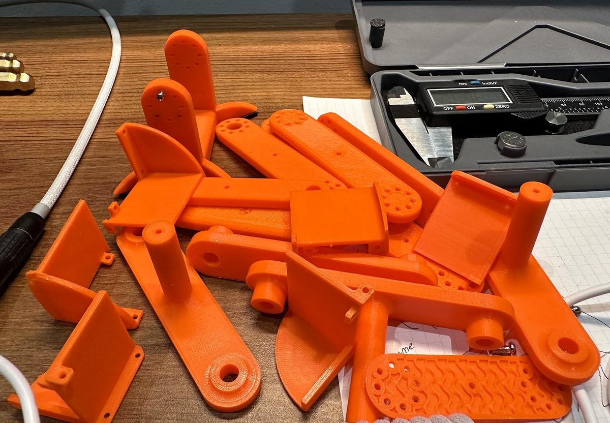 A pile of orange printed parts next to a digital caliper, some warped or failed.